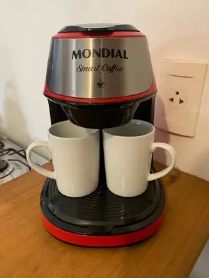 Mondial Smart Coffee vista de frente, apoiada em cima de mesa de madeira com duas xícaras brancas na base.