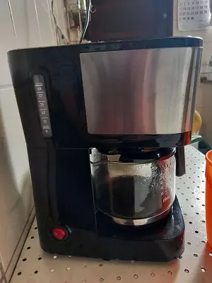 Oster OCAF300 vista de lado, apoiada em balcão de cozinha, com café em menos da metade da jarra de vidro.