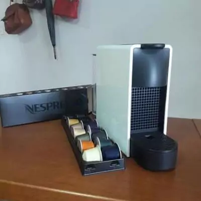 Nespresso Essenza Mini vista de frente sobre mesa de madeira com fileira de cápsulas ao lado esquerdo.