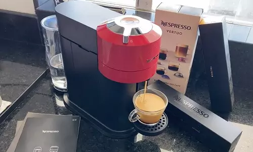 Nespresso Vertuo Next vista de cima em cima de balcão preto, com xícara de café cheia apoiada e sua embalagem atrás.