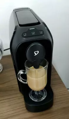 Três Corações TRES Passione em cima de balcão ligada, com xícara de café com leite cheia apoiada.