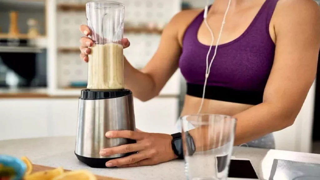 Mulher preparando um shake de academia no mini liquidificador portátil